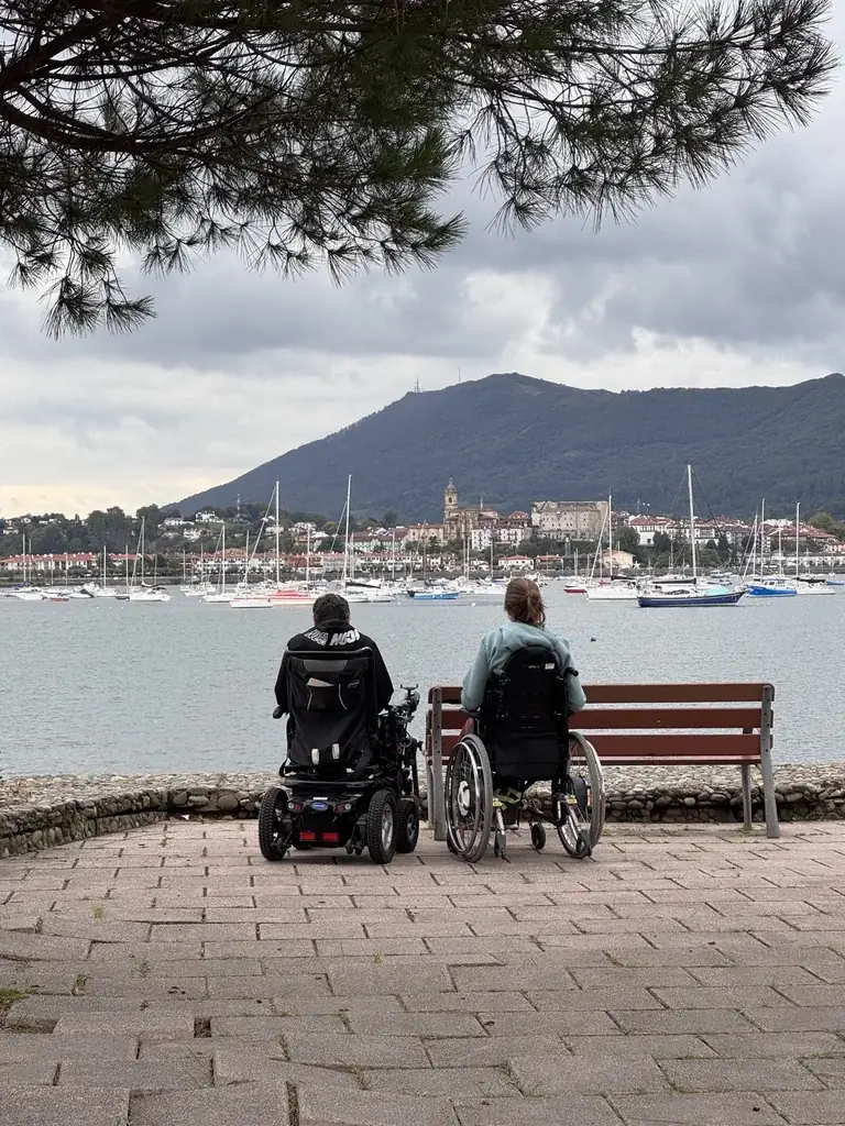 Deux personnes en fauteuil roulant, de dos, face au port d'Hendaye et à la montagne